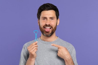 Happy man showing tongue cleaner on violet background