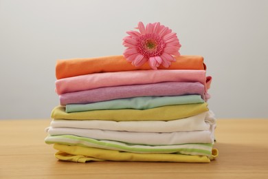 Photo of Stack of clean clothes and pink flower on wooden table