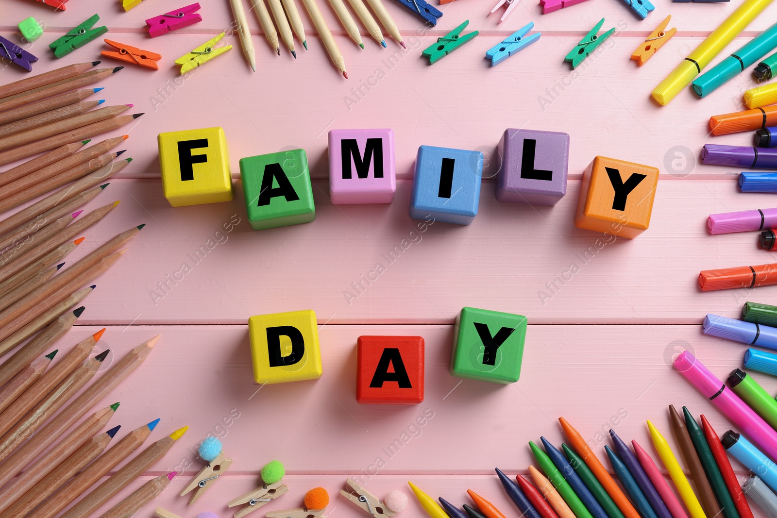 Photo of International Family day. Flat lay composition with cubes, pencils, crayons and clothespins on pink wooden background