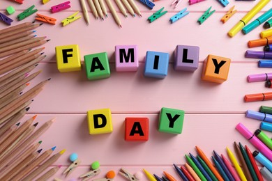 Photo of International Family day. Flat lay composition with cubes, pencils, crayons and clothespins on pink wooden background