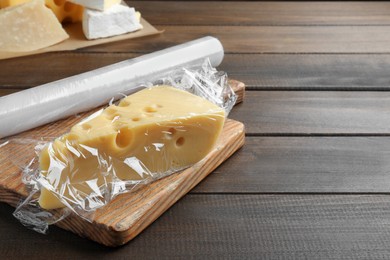 Photo of Block of cheese with plastic food wrap on wooden table. Space for text