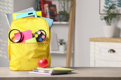 Photo of Yellow backpack and different school stationery on table indoors, space for text