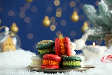 Photo of Different decorated Christmas macarons on table with artificial snow against blurred lights