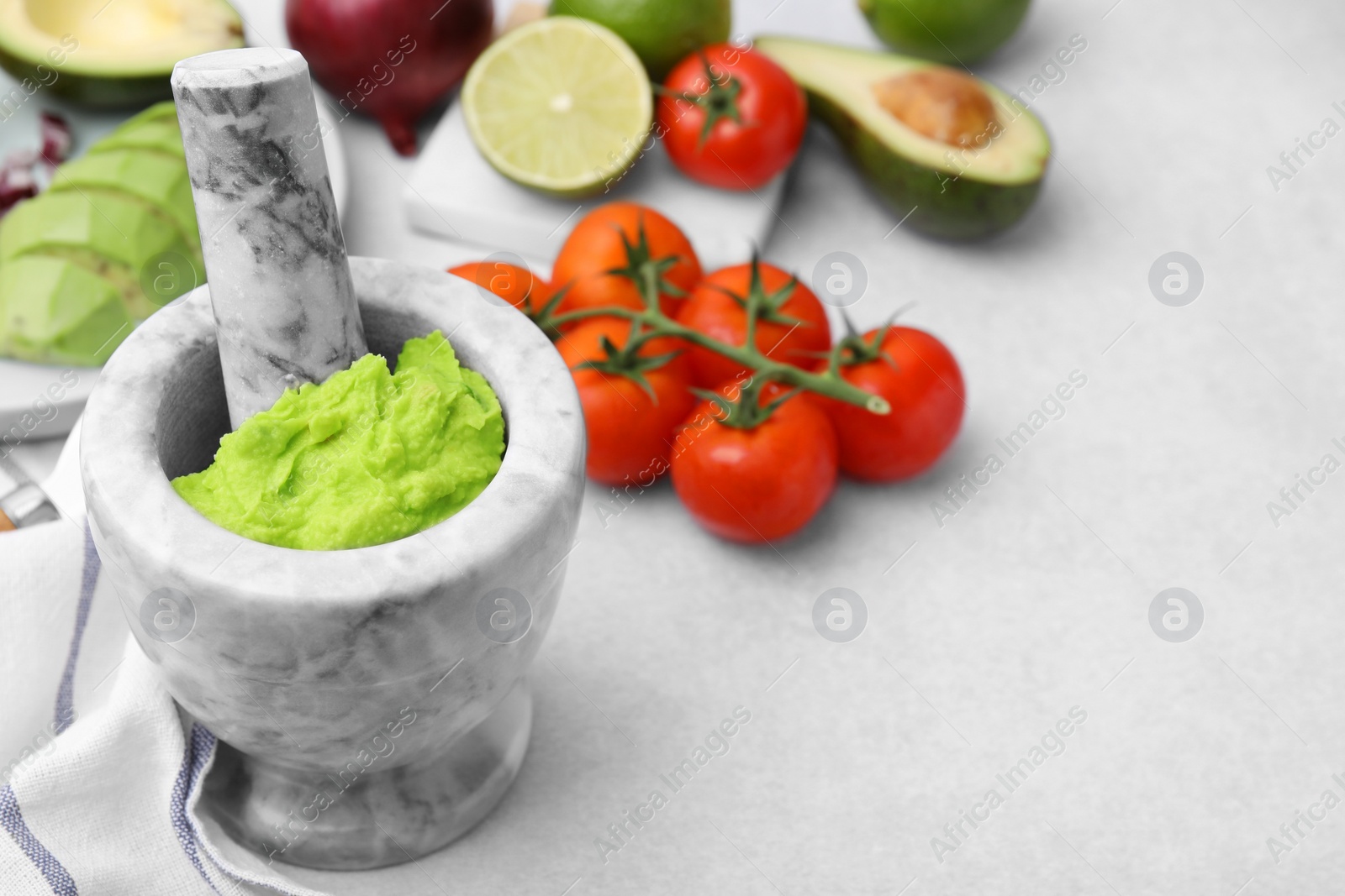 Photo of Mortar with delicious guacamole and ingredients on white table, closeup. Space for text