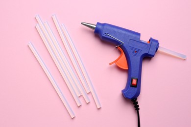 Blue glue gun and sticks on pink background, flat lay