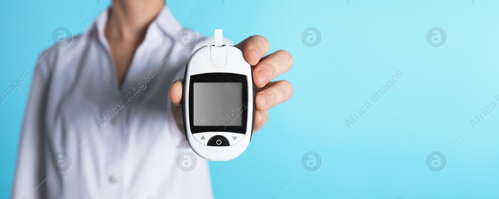 Image of Endocrinologist holding digital glucometer on light blue background, closeup. Banner design with space for text