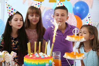 Happy children near cake with firework candles at birthday party indoors