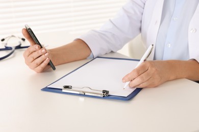Photo of Doctor with smartphone and clipboard at desk indoors, closeup. Online medicine concept