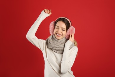 Photo of Happy woman wearing warm earmuffs on red background