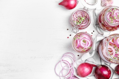 Flat lay composition with jars of pickled onions on white wooden table. Space for text