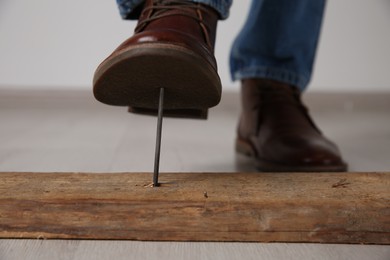 Photo of Careless man stepping on nail in wooden plank indoors, closeup