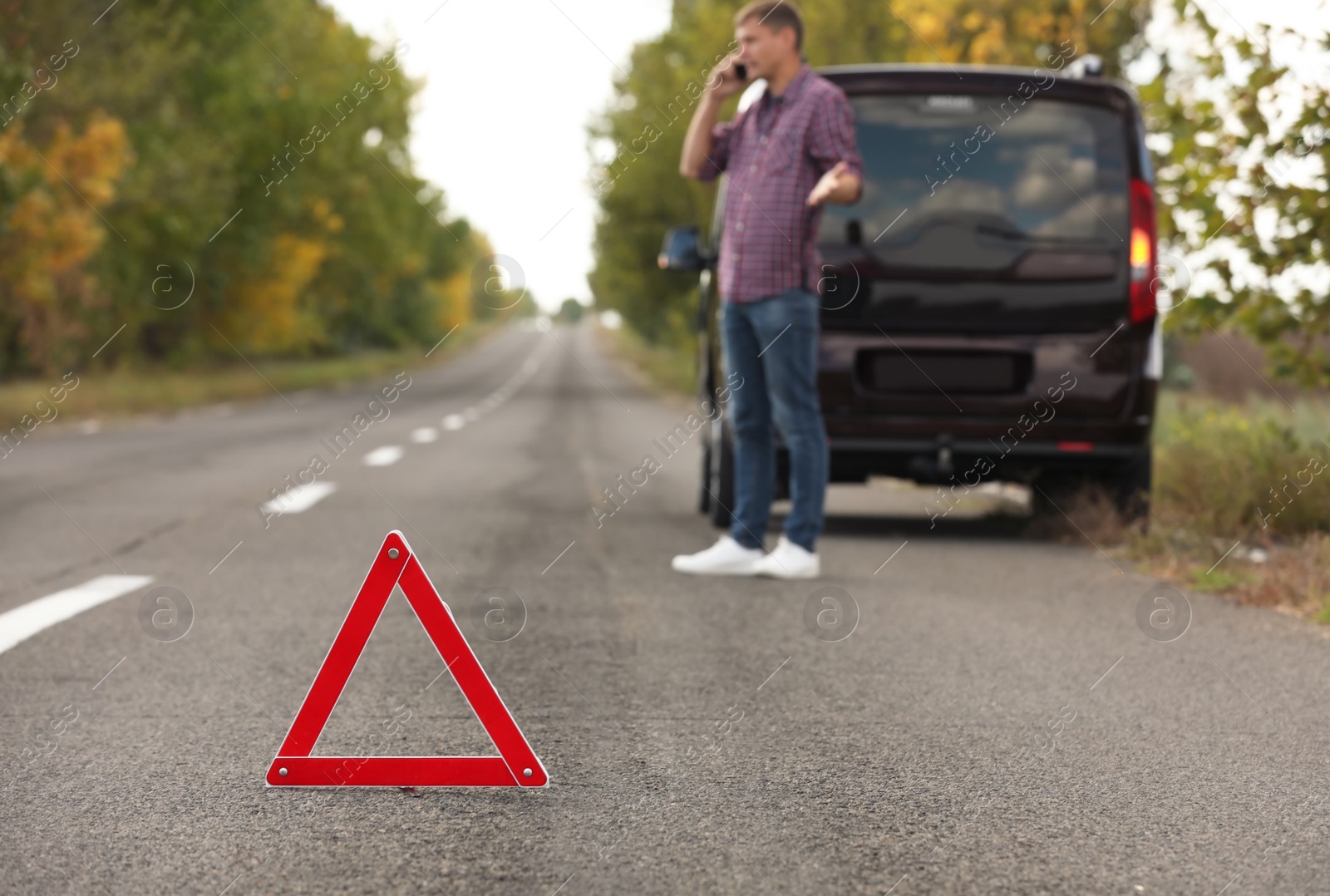 Photo of Emergency stop sign and driver near broken car on road. Auto insurance