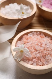 Photo of Different types of sea salt and flowers on light table, selective focus. Spa products