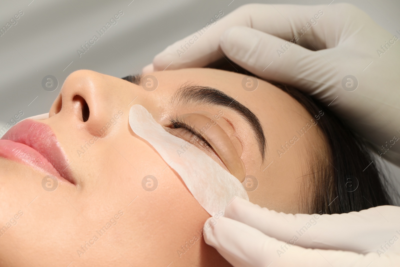 Photo of Young woman undergoing eyelash lamination, closeup. Professional service