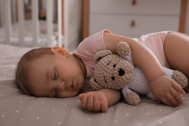 Photo of Adorable little baby with toy bear sleeping on bed at home