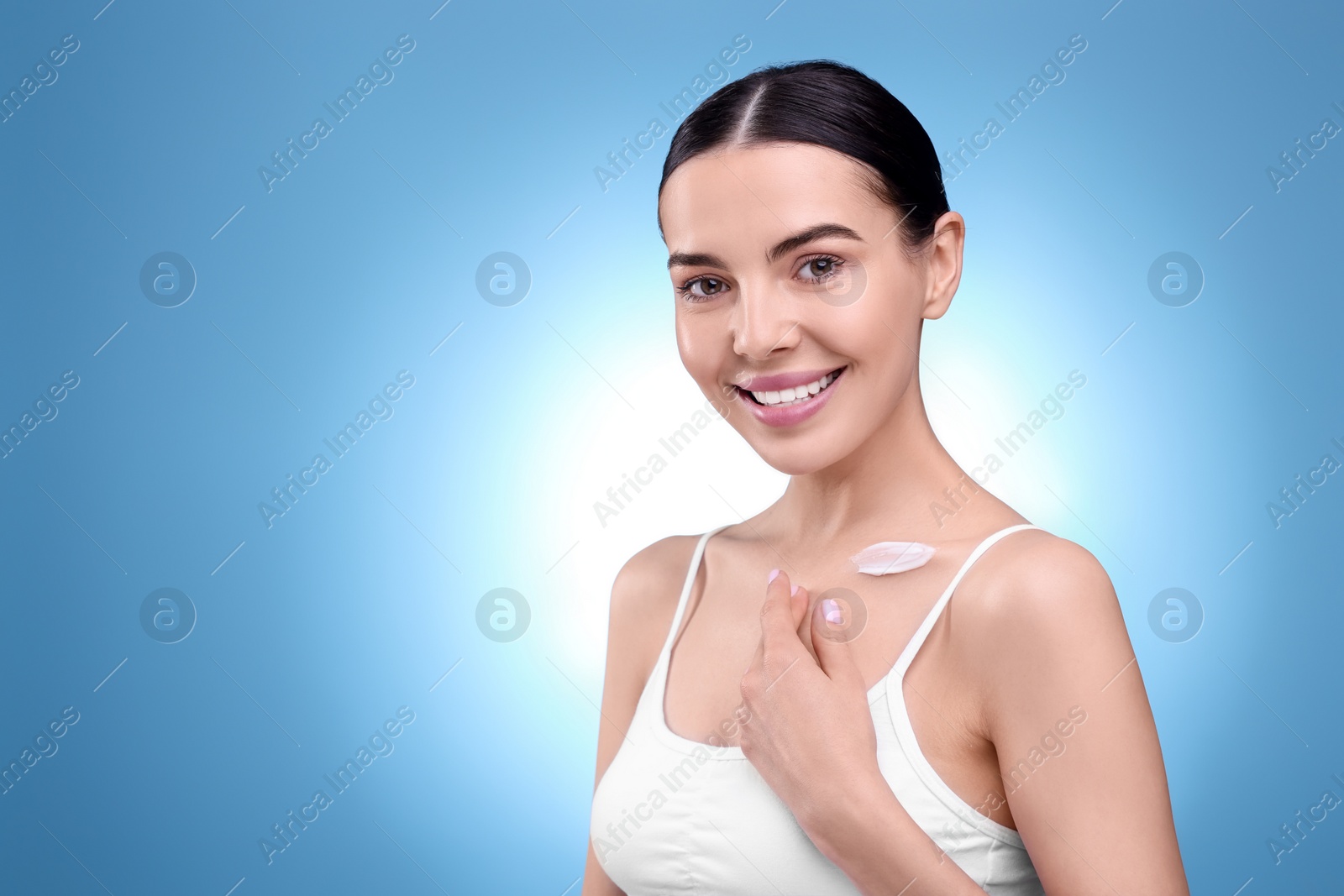 Photo of Beautiful woman with smear of body cream on her collarbone against light blue background, space for text