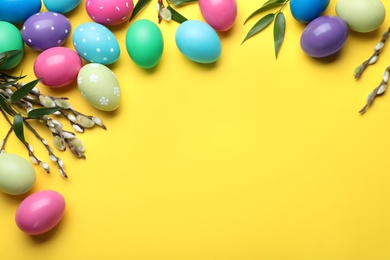 Photo of Bright painted eggs and pussy willows on yellow background, flat lay with space for text. Happy Easter