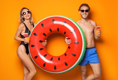 Photo of Happy young couple in beachwear with inflatable ring and cocktails on color background