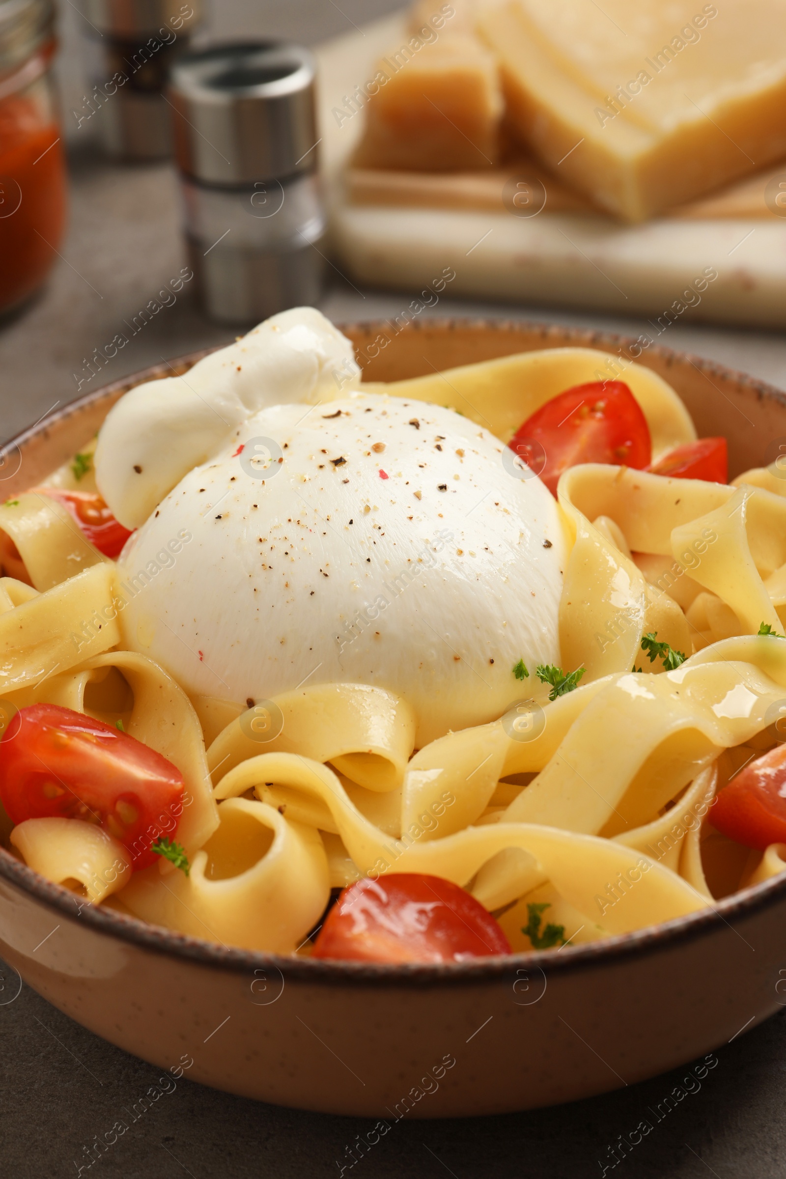 Photo of Bowl of delicious pasta with burrata and tomatoes on grey table, closeup