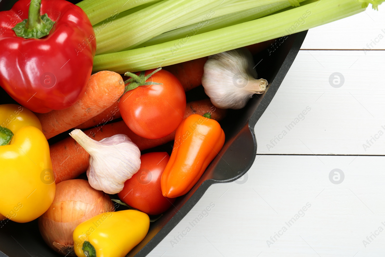 Photo of Black pot with fresh vegetables on white wooden table, top view. Space for text