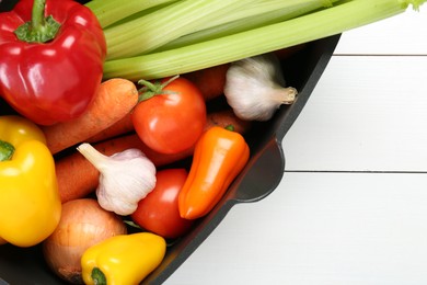 Photo of Black pot with fresh vegetables on white wooden table, top view. Space for text