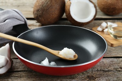 Frying pan with organic coconut cooking oil and spoon on wooden table, closeup