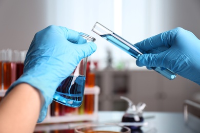 Scientist holding tube and conical flask at laboratory, closeup. Solution chemistry