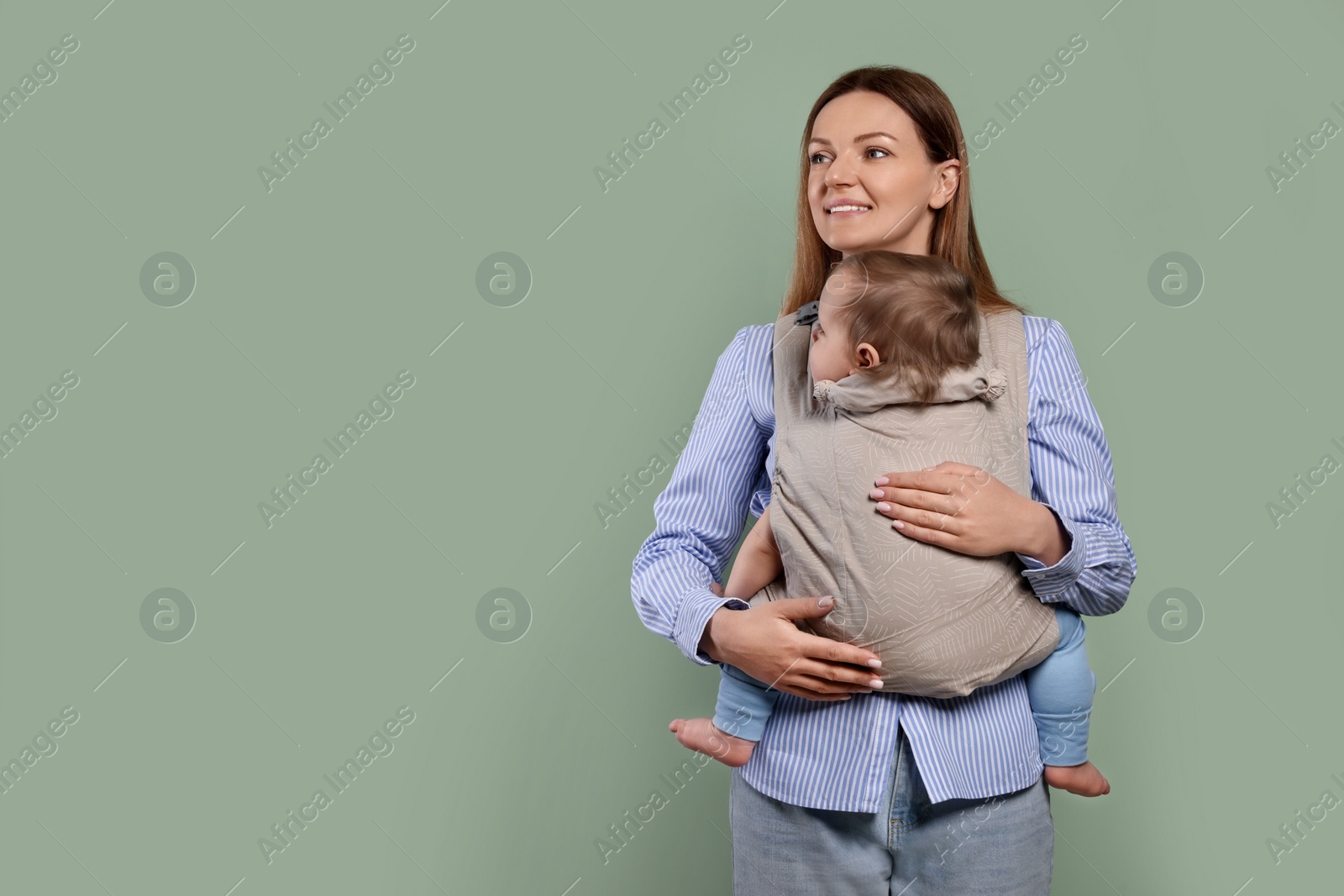 Photo of Mother holding her child in sling (baby carrier) on olive background