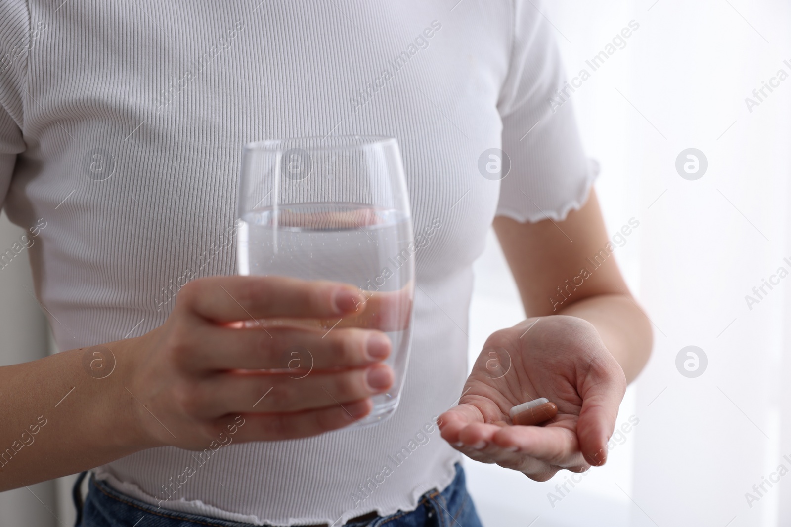 Photo of Woman with vitamin pills and glass of water indoors, closeup