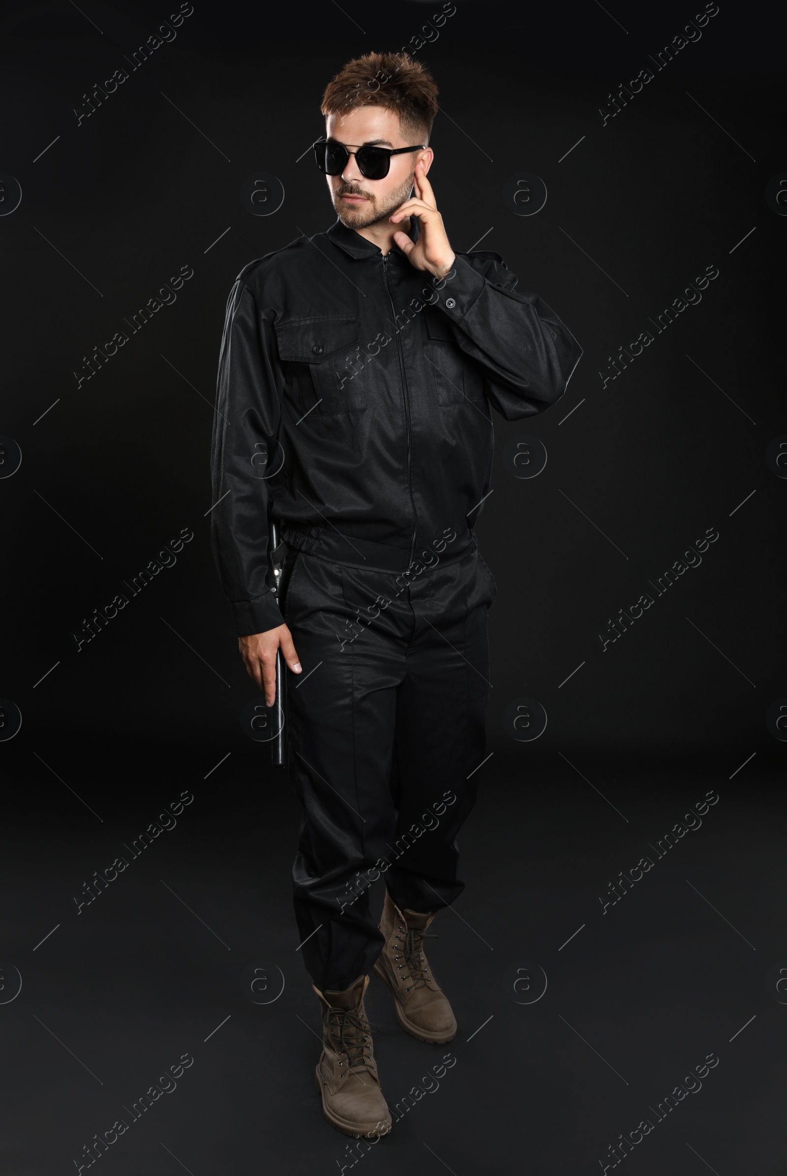 Photo of Male security guard in uniform using radio earpiece on dark background