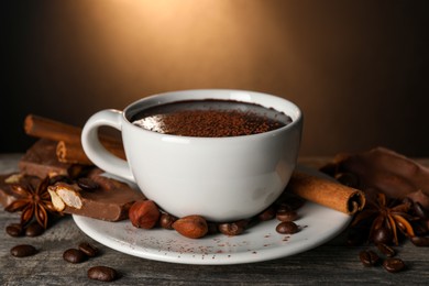 Cup of delicious hot chocolate, spices and coffee beans on wooden table