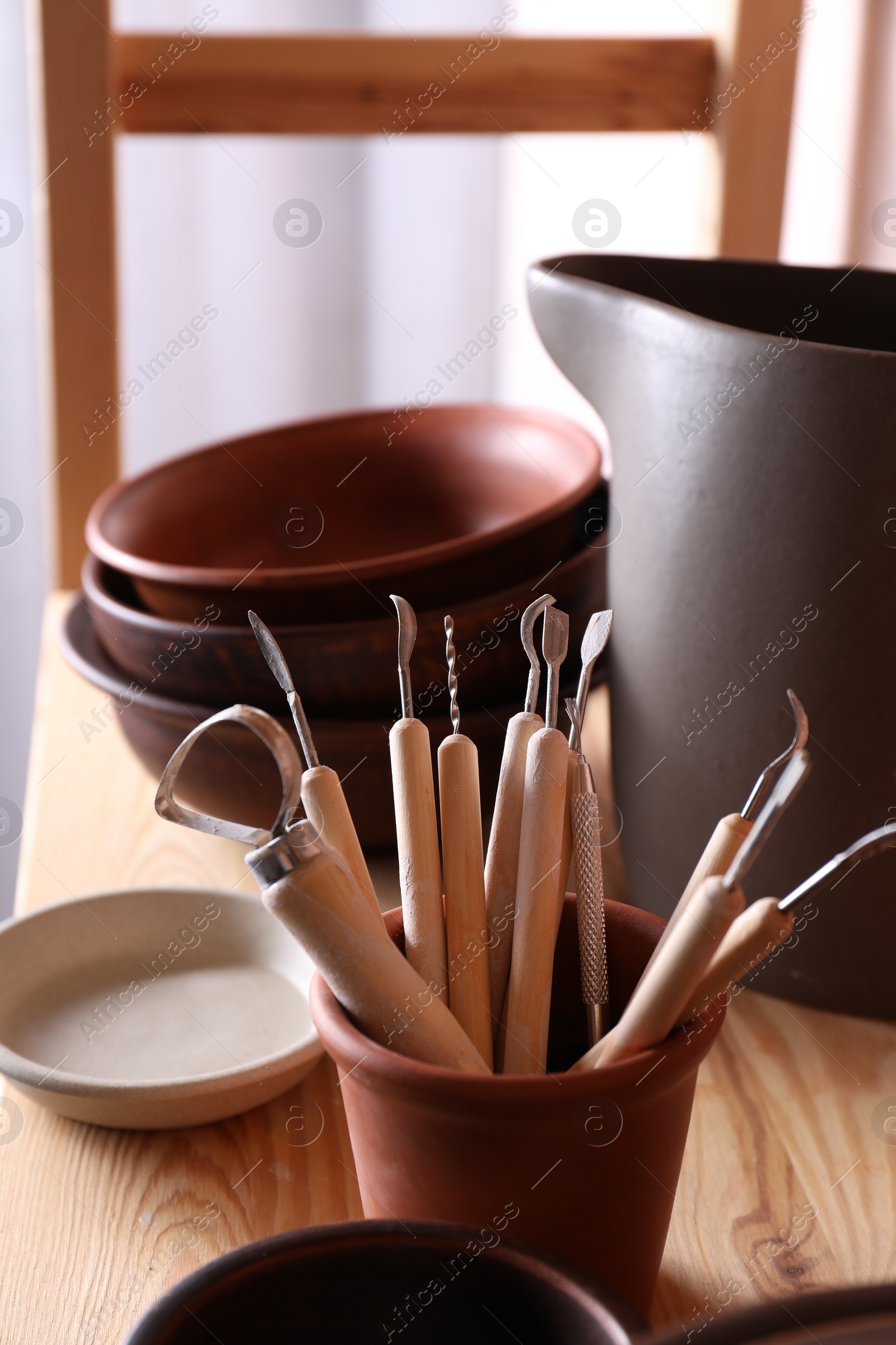 Photo of Set of different crafting tools and clay dishes on wooden table in workshop