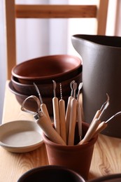 Set of different crafting tools and clay dishes on wooden table in workshop