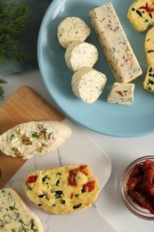 Photo of Different types of tasty butter, dill, chili peppers and bread on white table, flat lay