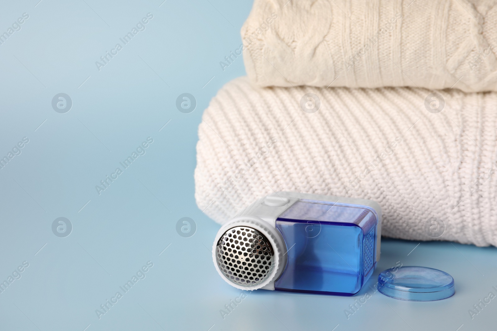 Photo of Modern fabric shaver and knitted clothes on light blue background, space for text