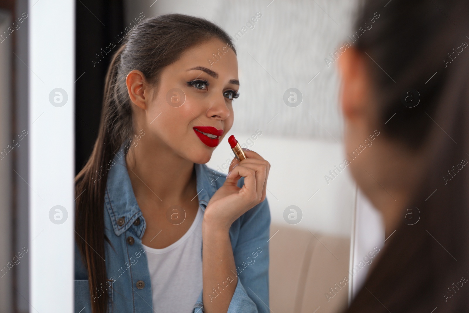 Photo of Beautiful woman applying red lipstick near mirror