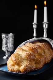Photo of Homemade braided bread with sesame seeds, goblet and candles on dark grey table, closeup. Traditional Shabbat challah