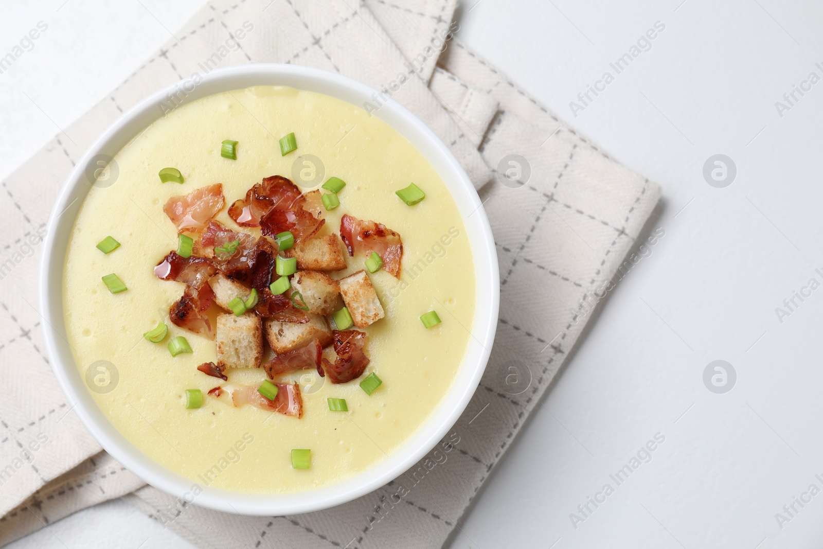 Photo of Tasty potato soup with bacon, green onion and croutons in bowl on white table, top view. Space for text