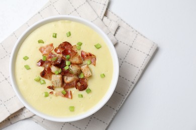 Tasty potato soup with bacon, green onion and croutons in bowl on white table, top view. Space for text