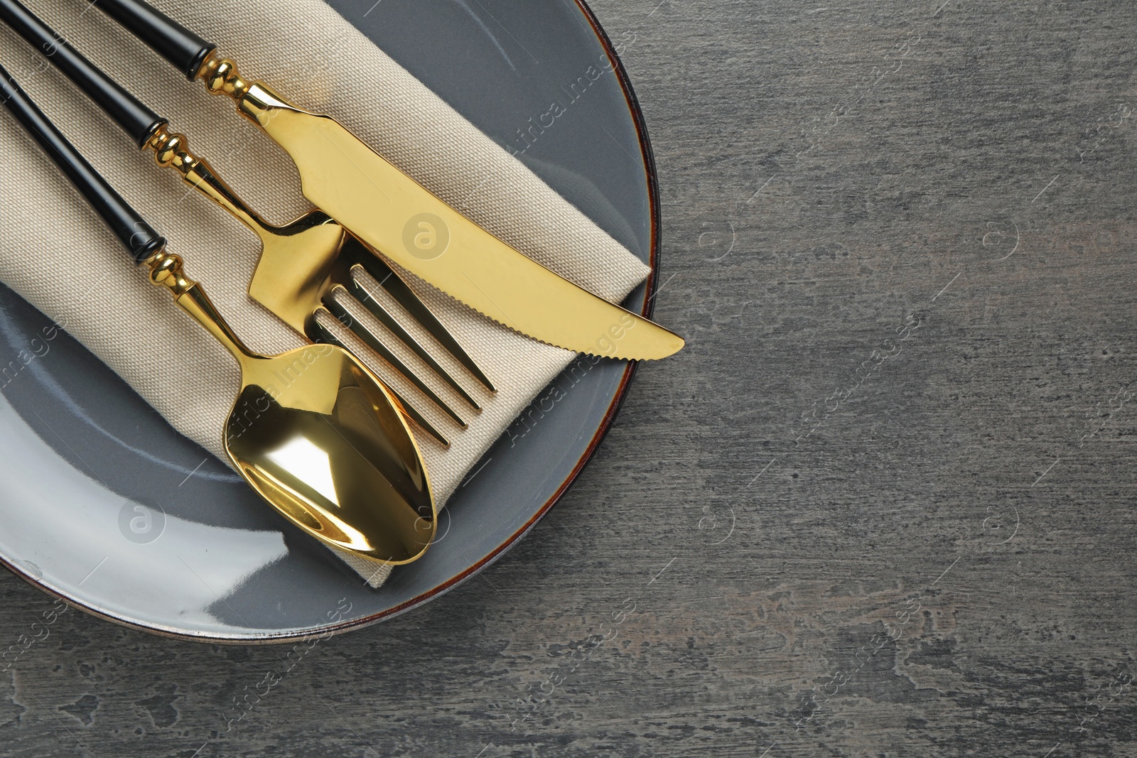 Photo of Elegant setting with golden cutlery on dark grey table, top view. Space for text