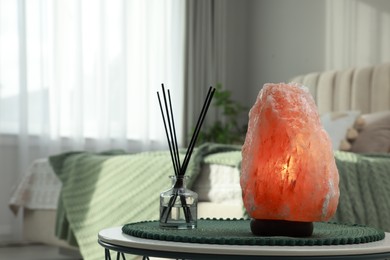 Beautiful Himalayan salt lamp and air reed freshener on table in bedroom, space for text