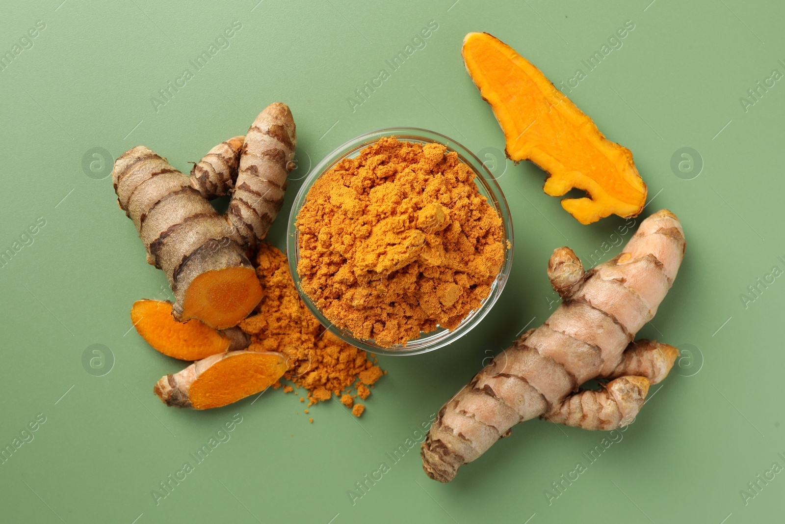 Photo of Aromatic turmeric powder and raw roots on green background, flat lay