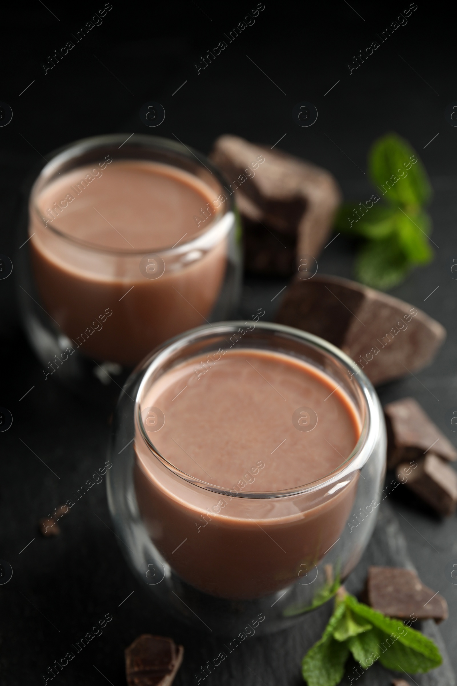 Photo of Glasses of delicious hot chocolate, chunks and fresh mint on black table