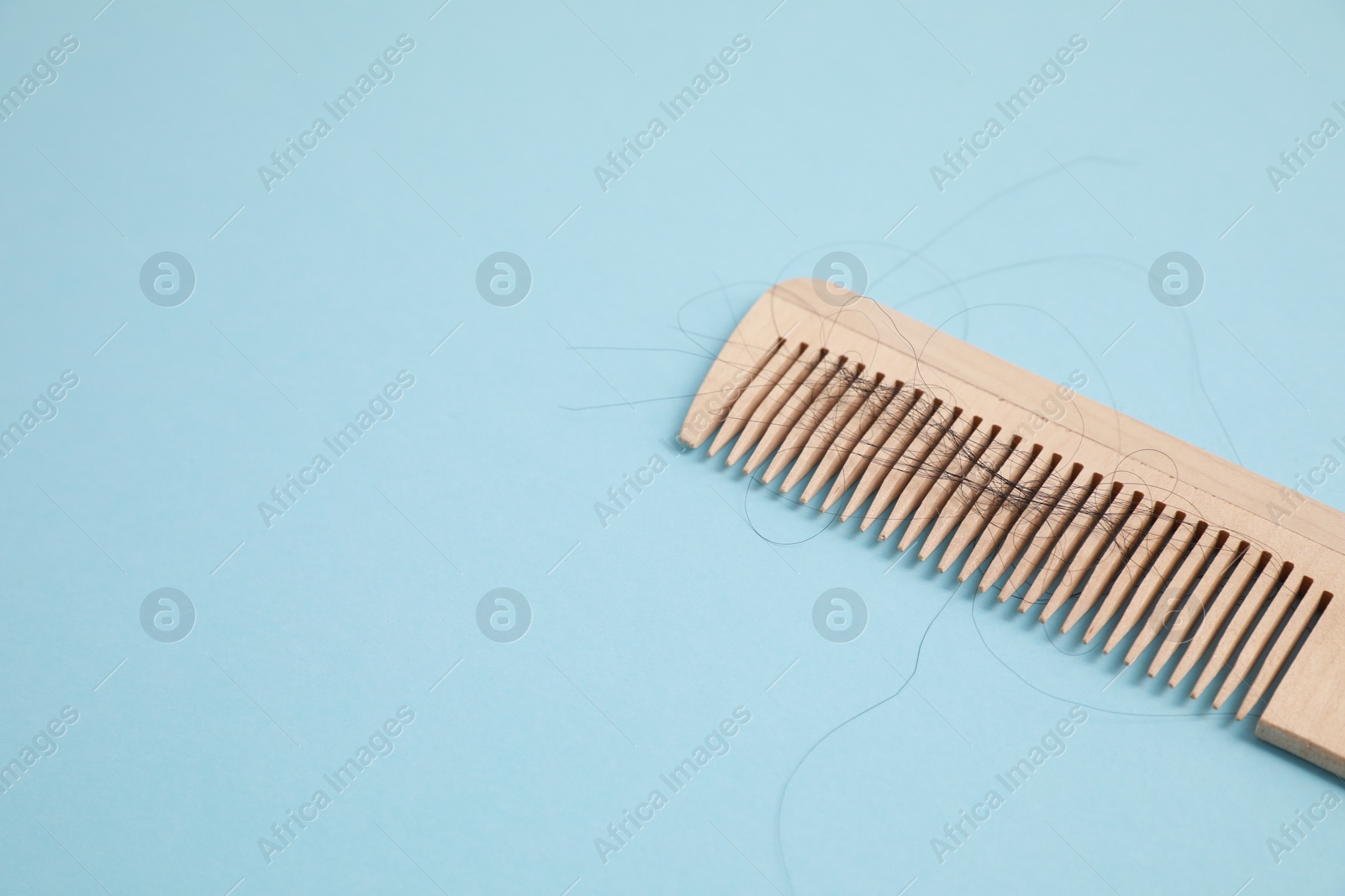 Photo of Wooden comb with lost hair on light blue background, closeup. Space for text