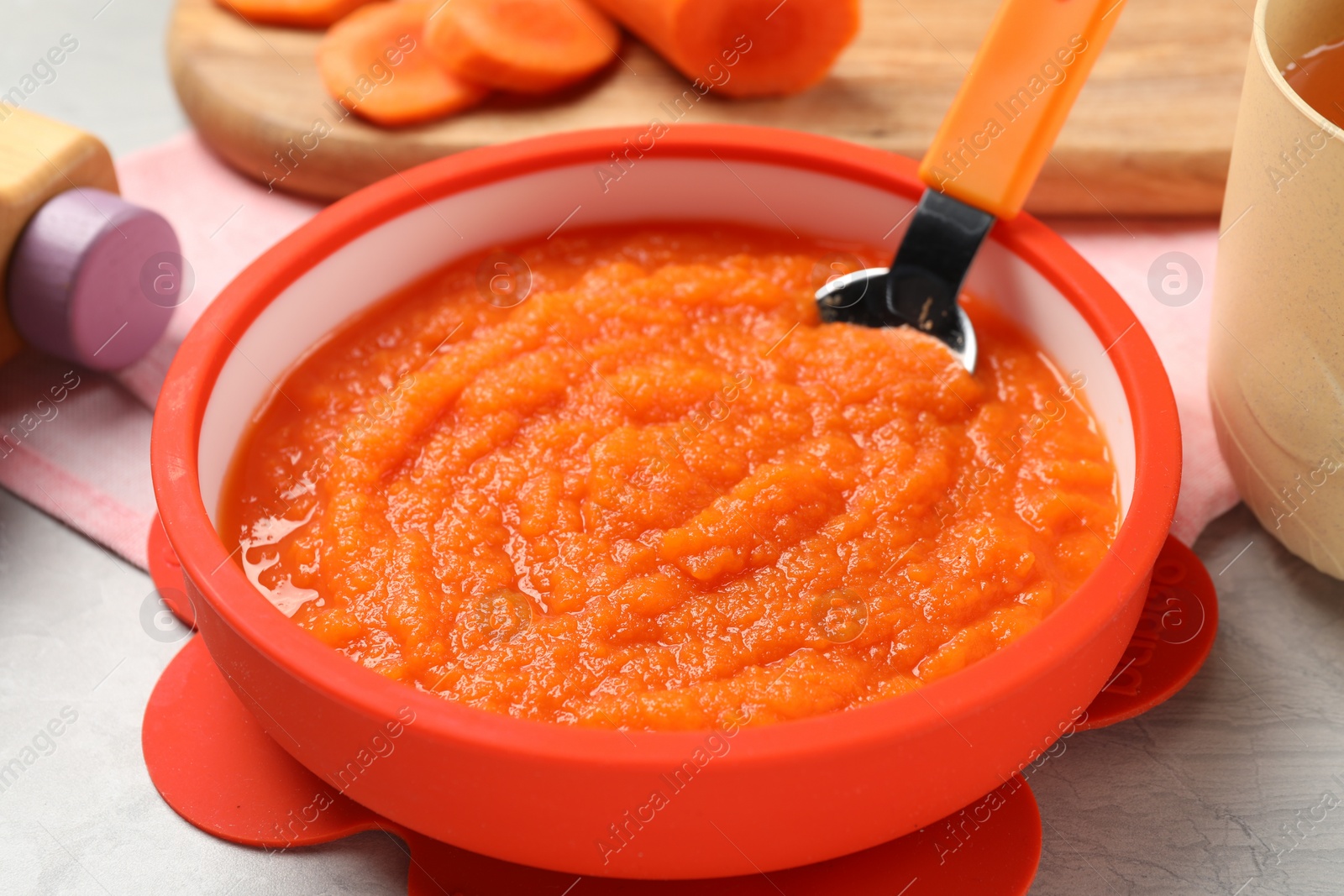 Photo of Healthy baby food. Bowl with delicious carrot puree on light grey marble table, closeup