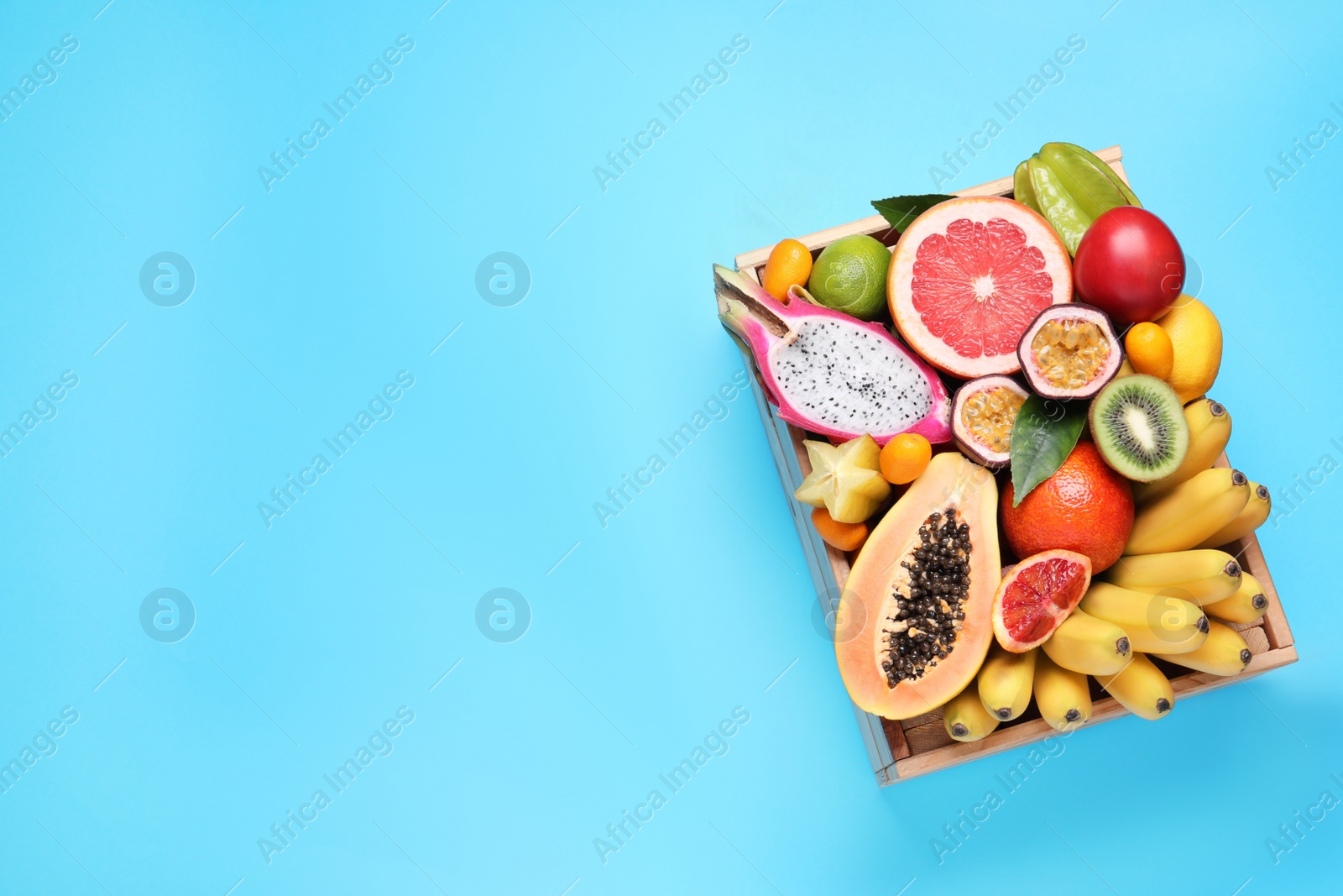 Photo of Crate with different exotic fruits on light blue background, top view. Space for text