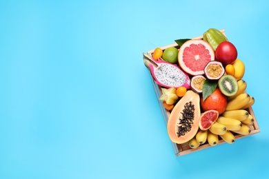 Crate with different exotic fruits on light blue background, top view. Space for text