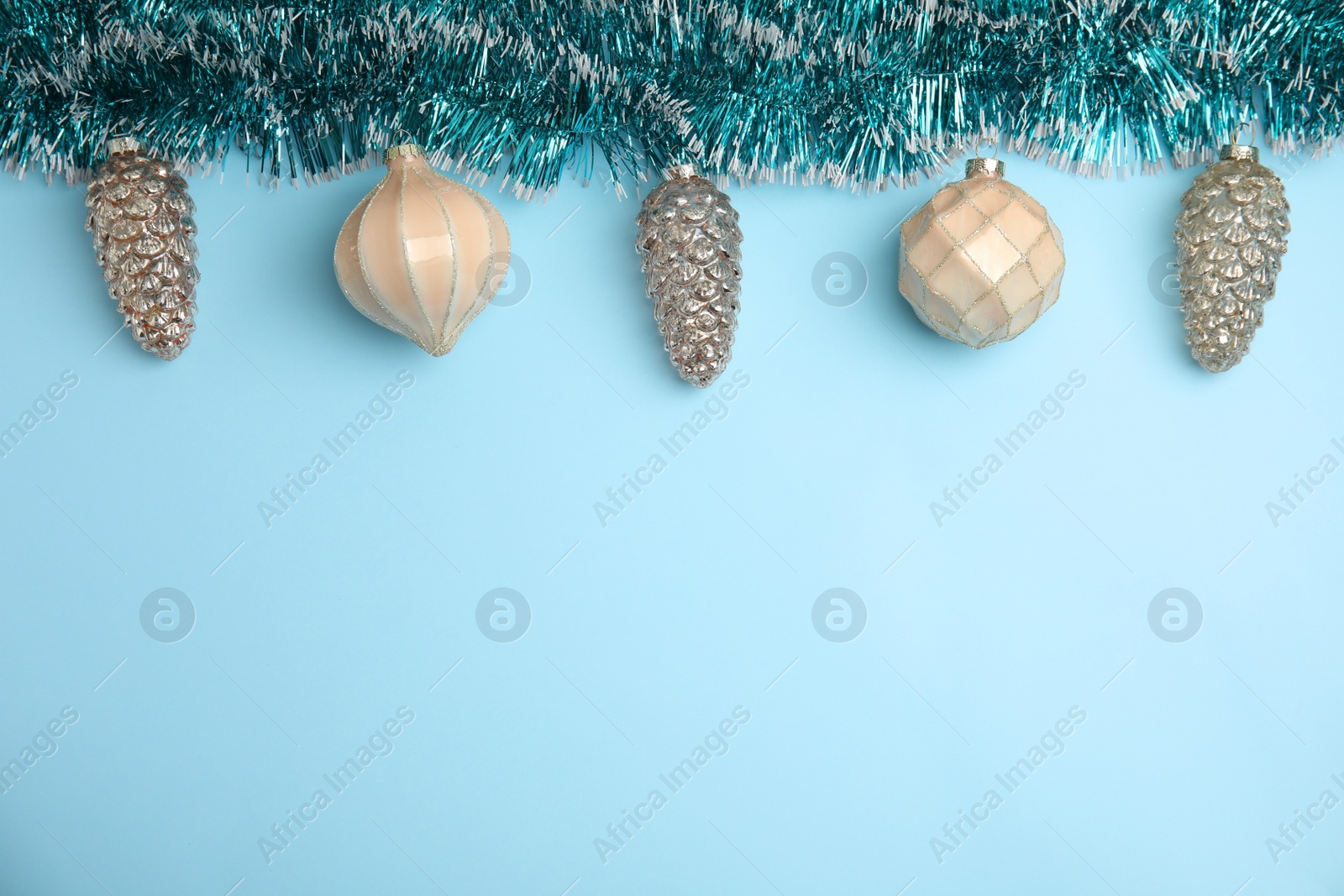 Photo of Shiny tinsel and Christmas balls on light blue background, flat lay. Space for text