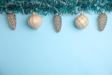 Photo of Shiny tinsel and Christmas balls on light blue background, flat lay. Space for text