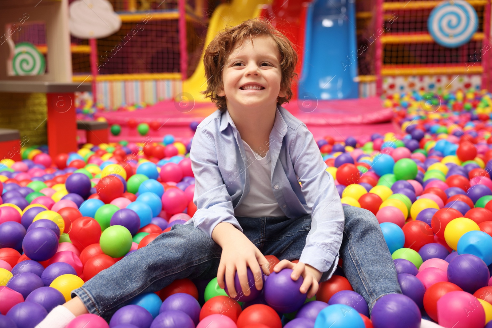 Photo of Happy little boy sitting on colorful balls in ball pit